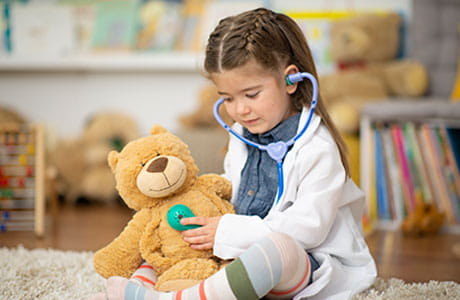 an image of a little girl using a stethoscope on a teddy bear