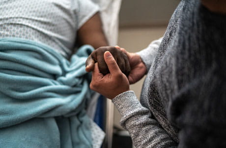 an image of a son holding a fathers hand at the hospital