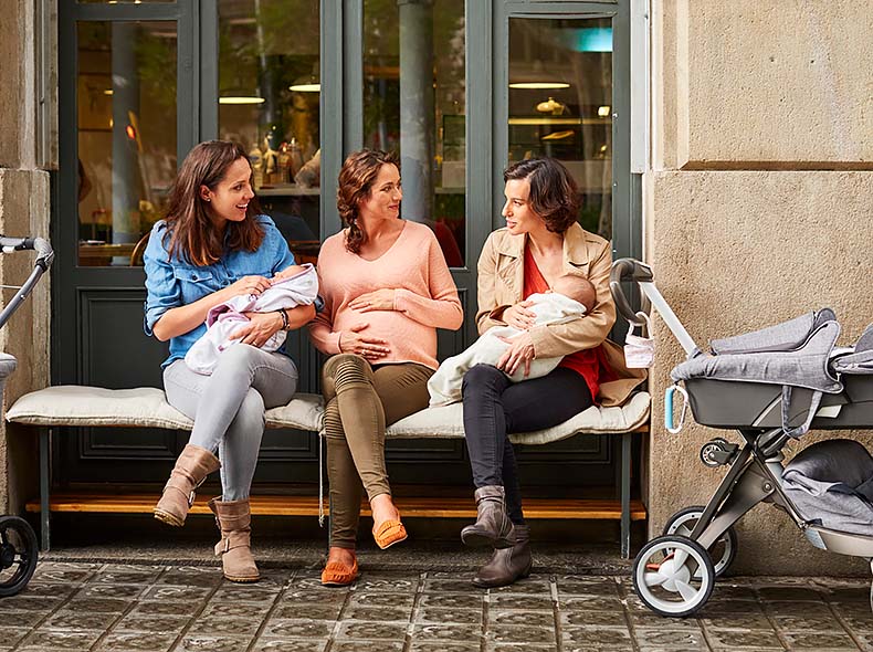 3 women sit on a bench discussing pregnancy, their babies, and other topics.